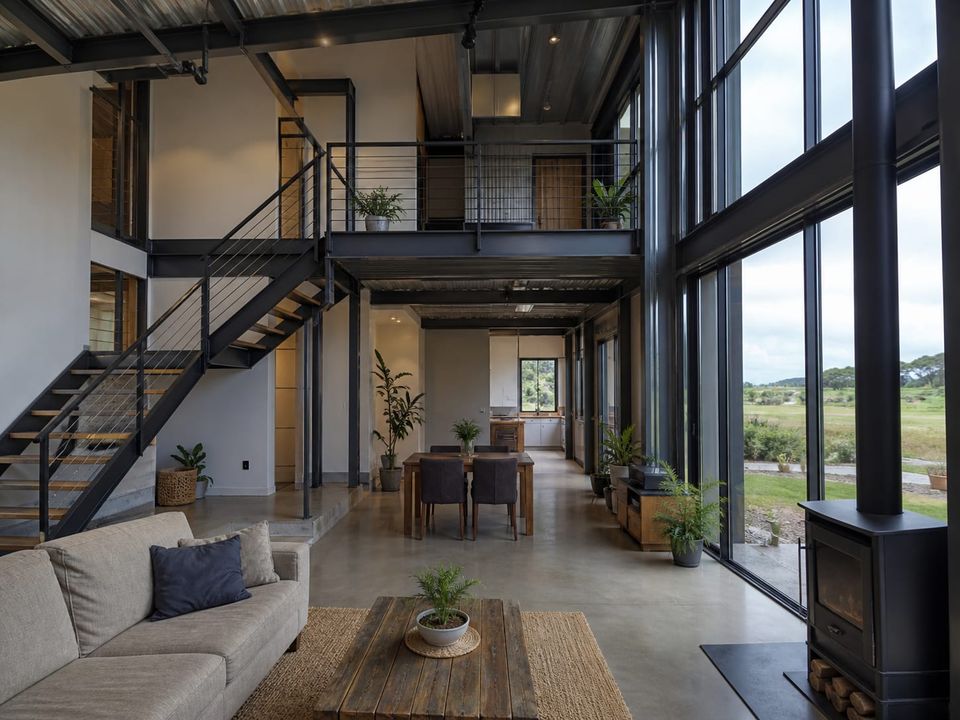 Two-storey steel home living space with tall glazing and open stair