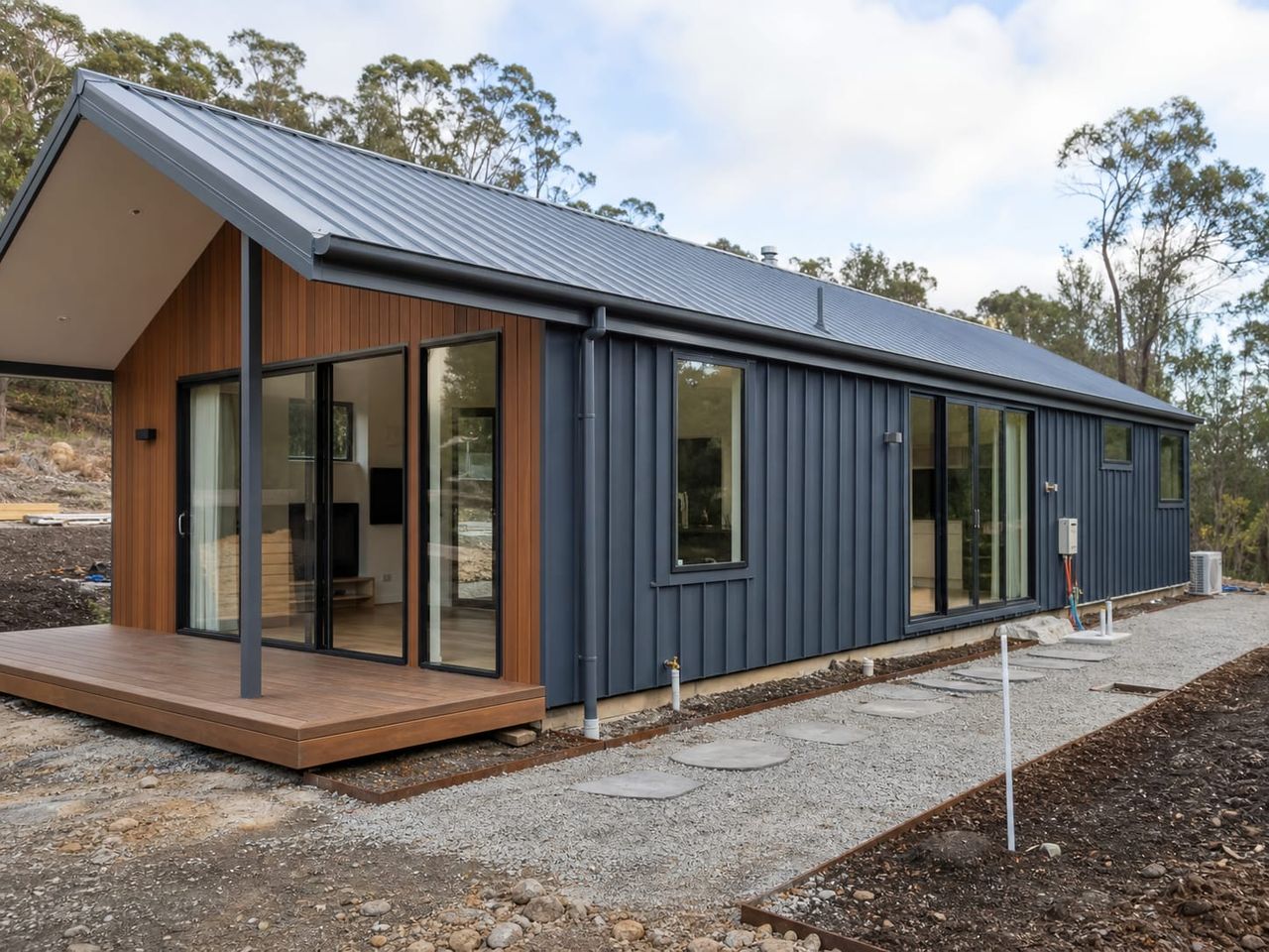 Single-storey steel home nearing completion with envelope, glazing, and external works