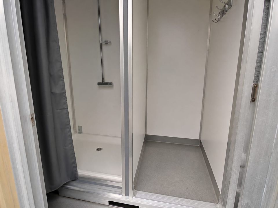Shower cubicle inside a sanitary container with tray, screening, and changing space